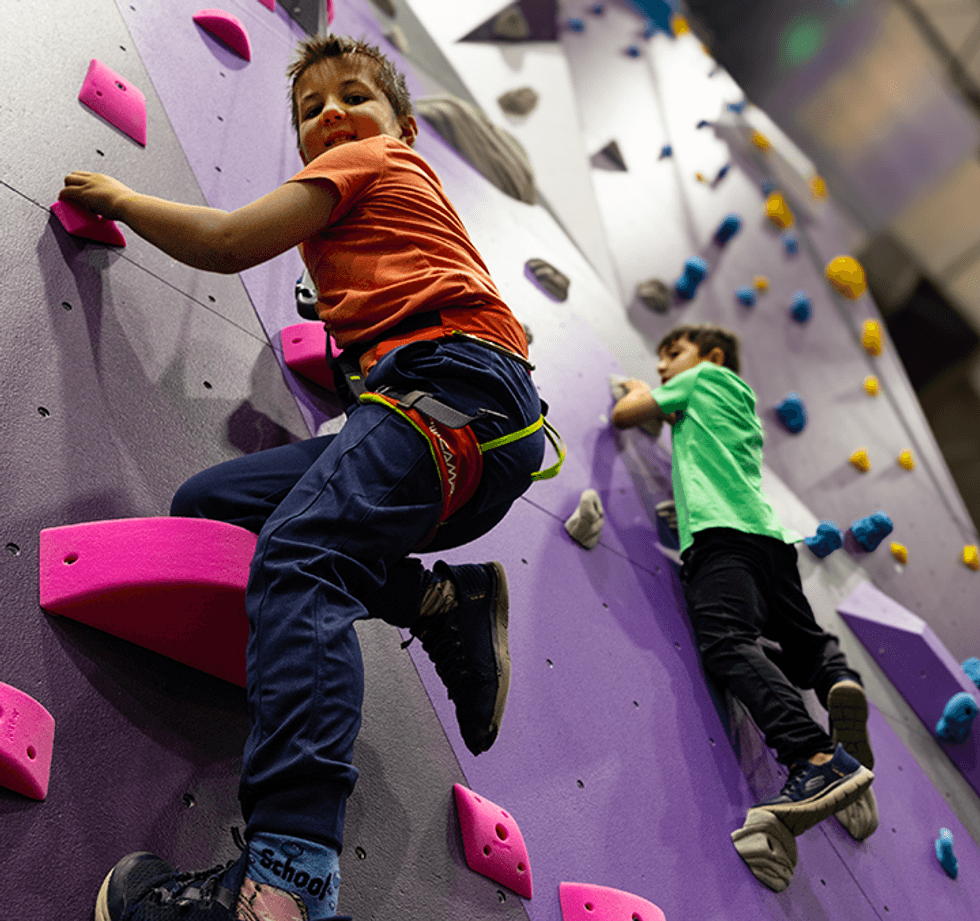 Two kids climbing a colorful indoor rock wall.