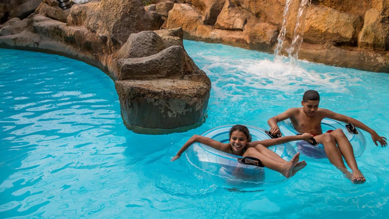 Two kids enjoying a lazy river ride in inflatable tubes near a rock waterfall at Alton Towers water park