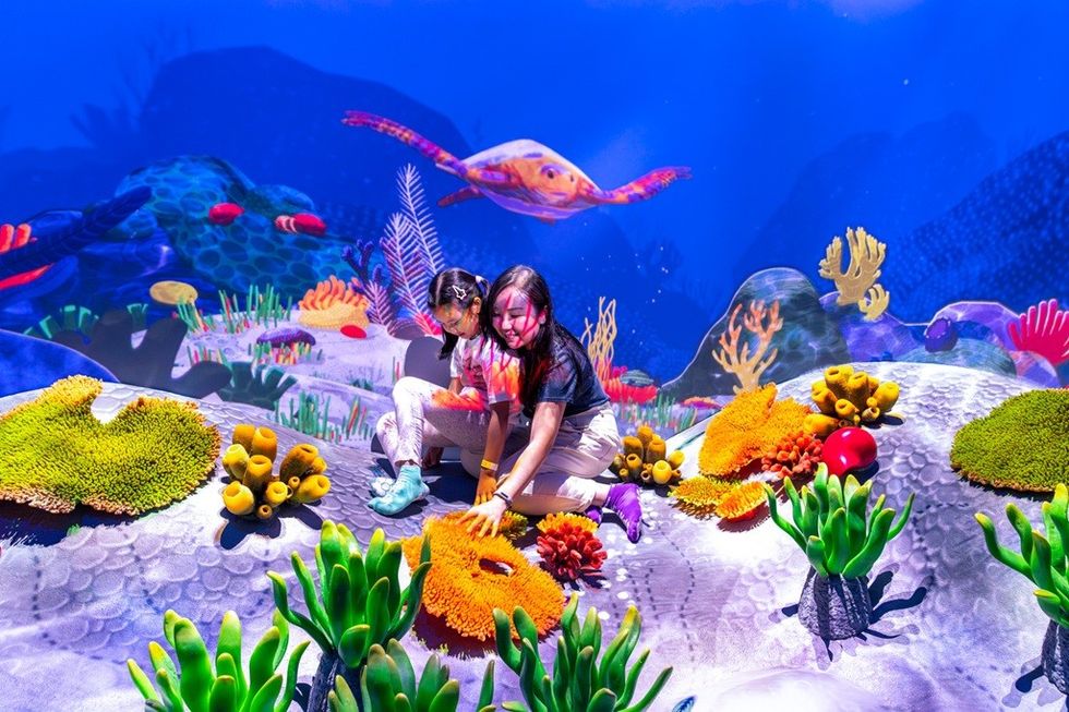 Two kids exploring a vibrant, interactive underwater exhibit with colorful corals and fish.