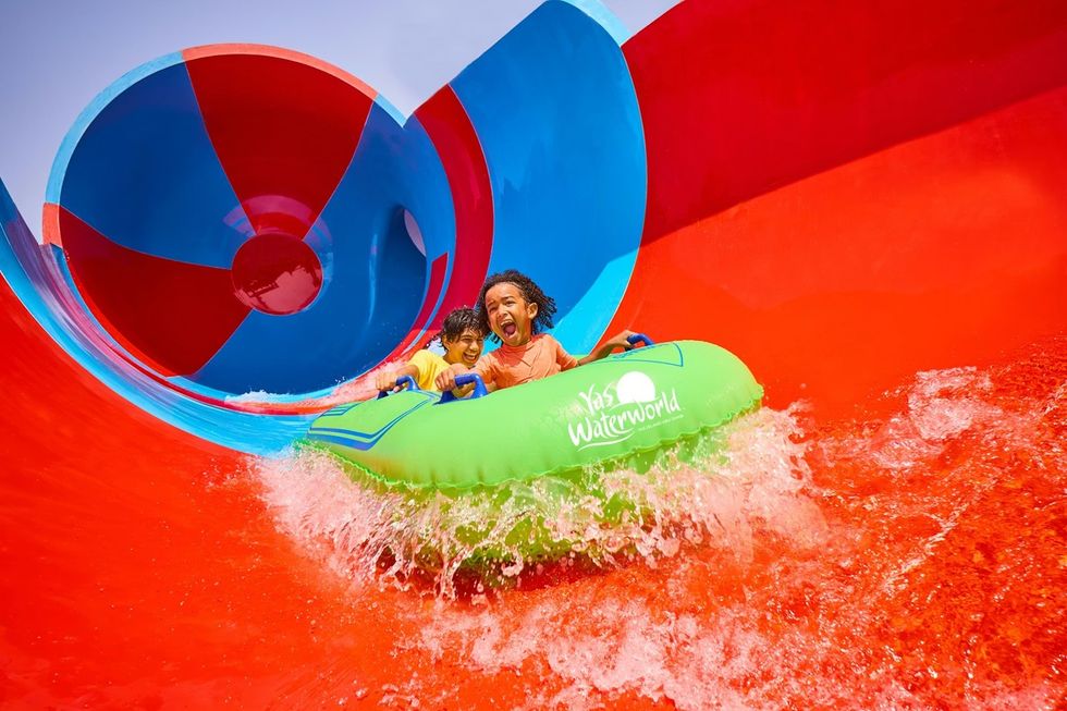 Two kids happily ride a green raft on a red and blue water slide at Yas Waterworld.