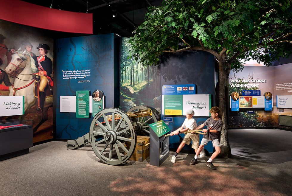 Two kids interact with an exhibit in a George Washington museum display.