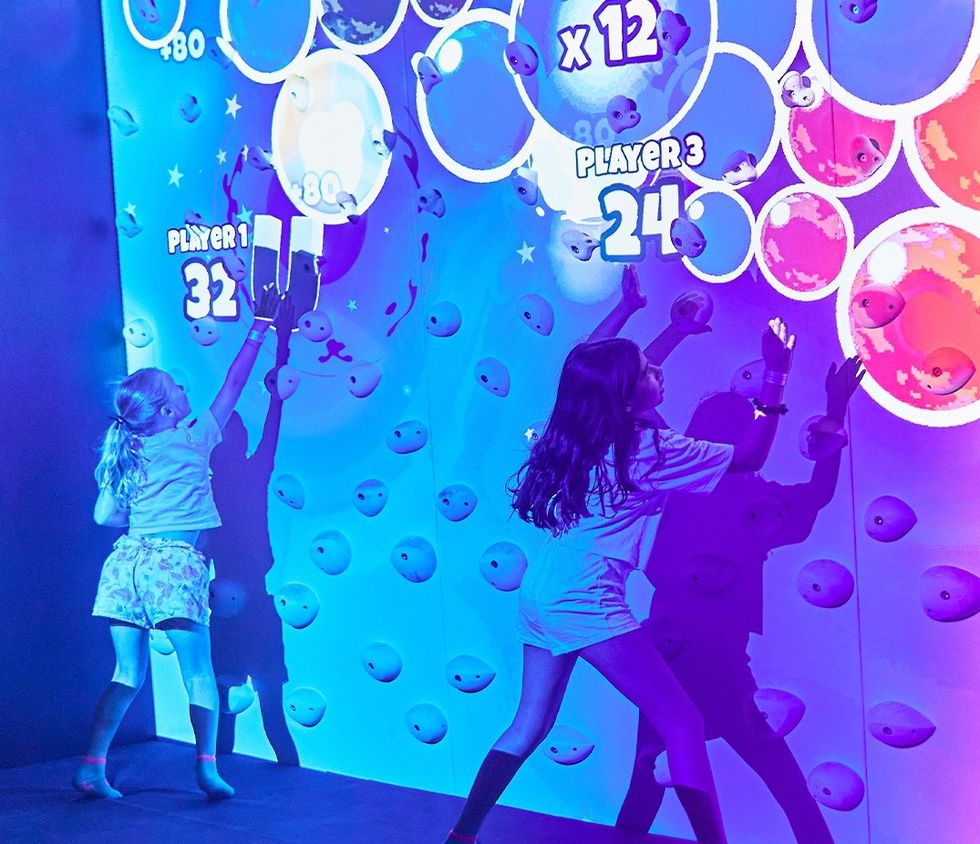 Two kids play on an interactive climbing wall with colorful projections.
