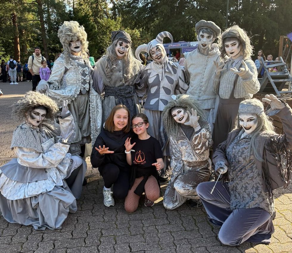 Two kids pose with costumed performers in medieval-style gray outfits.