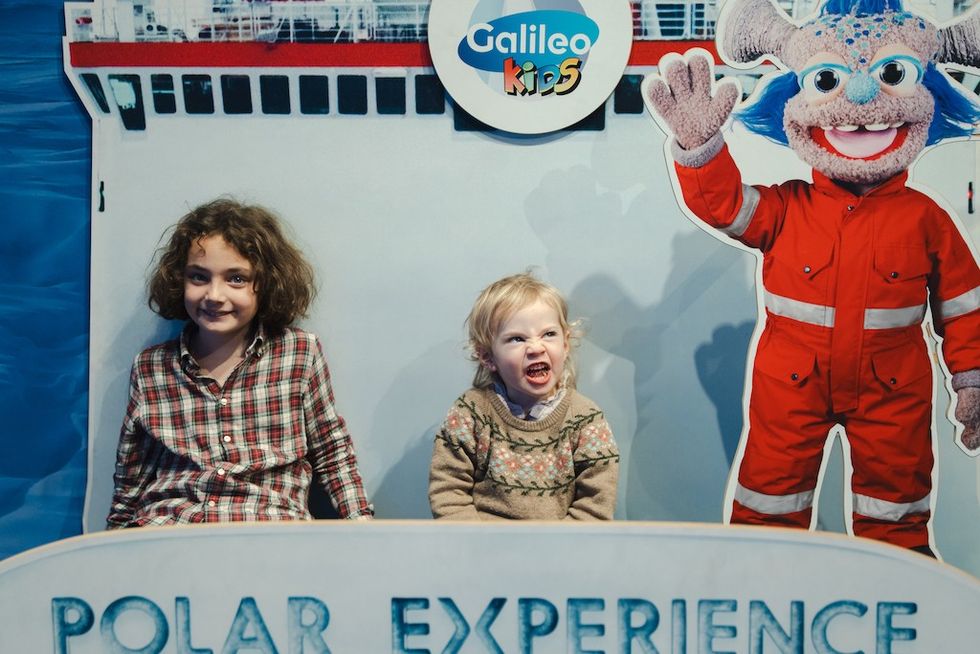 Two kids posing with a cutout of a mascot at a "Galileo Kids Polar Experience" display.