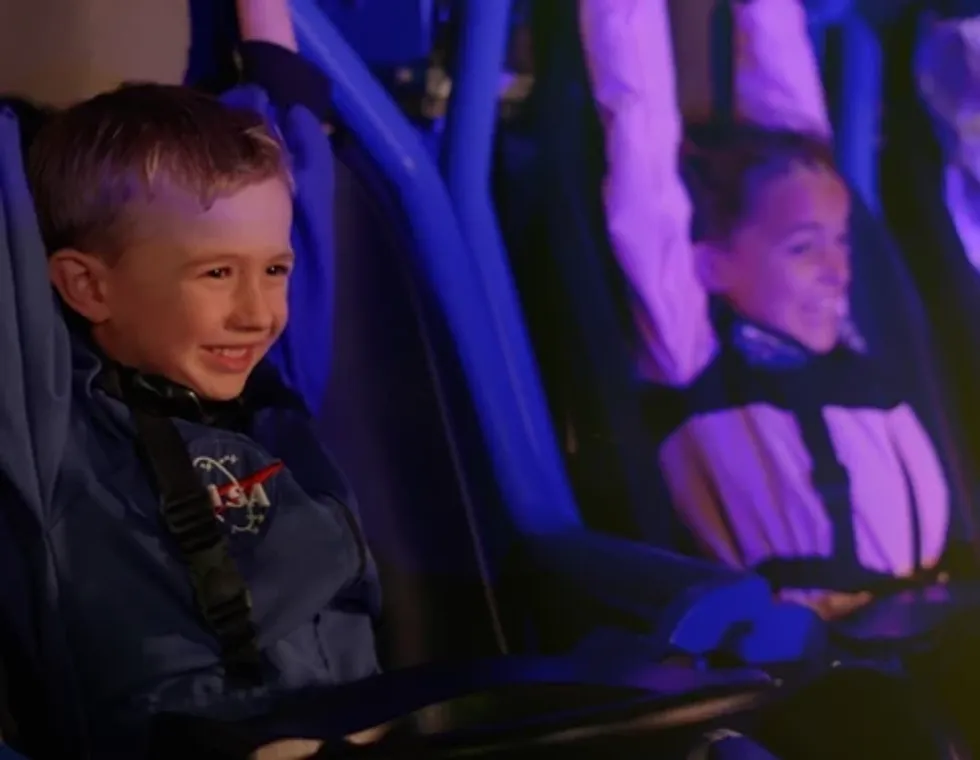 Two kids smiling in a space-themed ride with blue lighting.