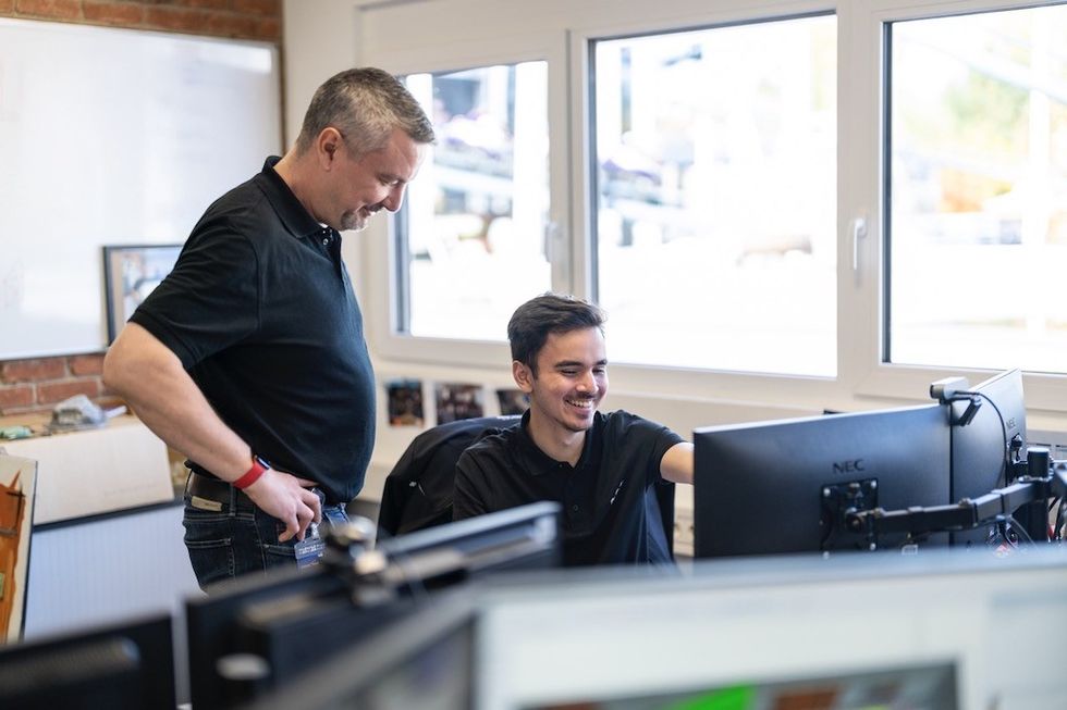 Two men in an office, smiling at a computer screen.
