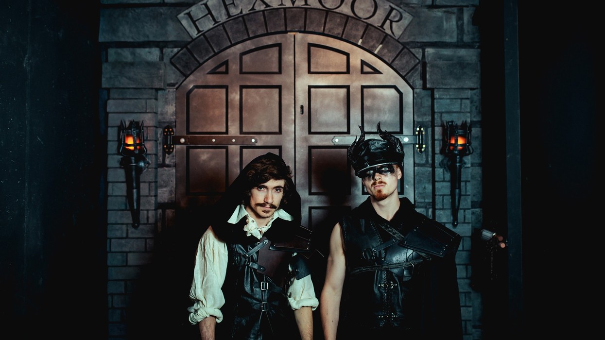 Two men in fantasy armor stand before the ornate doors of "Hexmoor," flanked by torches.