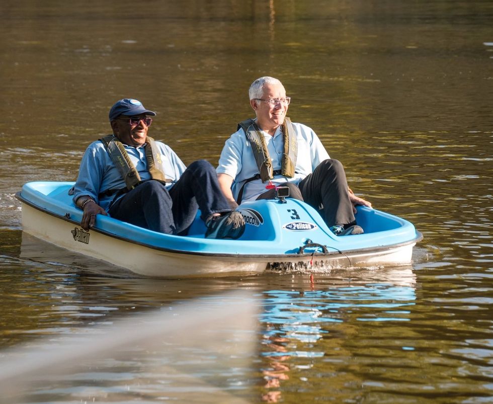 Two men in life vests enjoy a pedal boat ride on calm water.