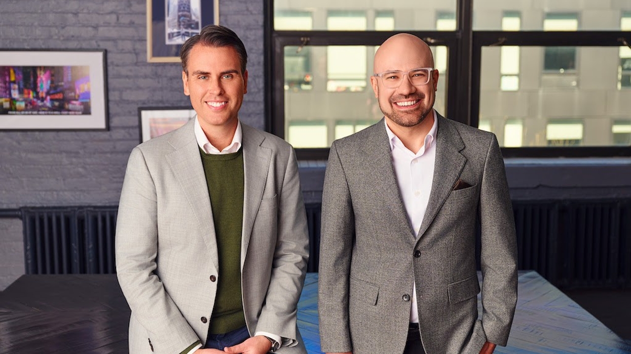 Two men in suits smiling in a modern office setting.