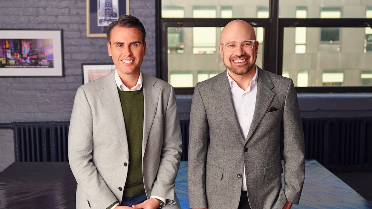 Two men in suits smiling in a modern office setting.