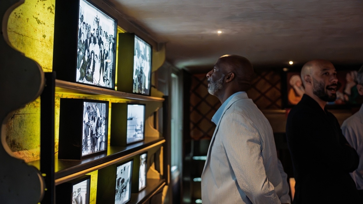 Two men observing illuminated vintage photos on a dimly lit gallery wall at the Edward W. Kane & Martha J. Wallace Center for Black History.