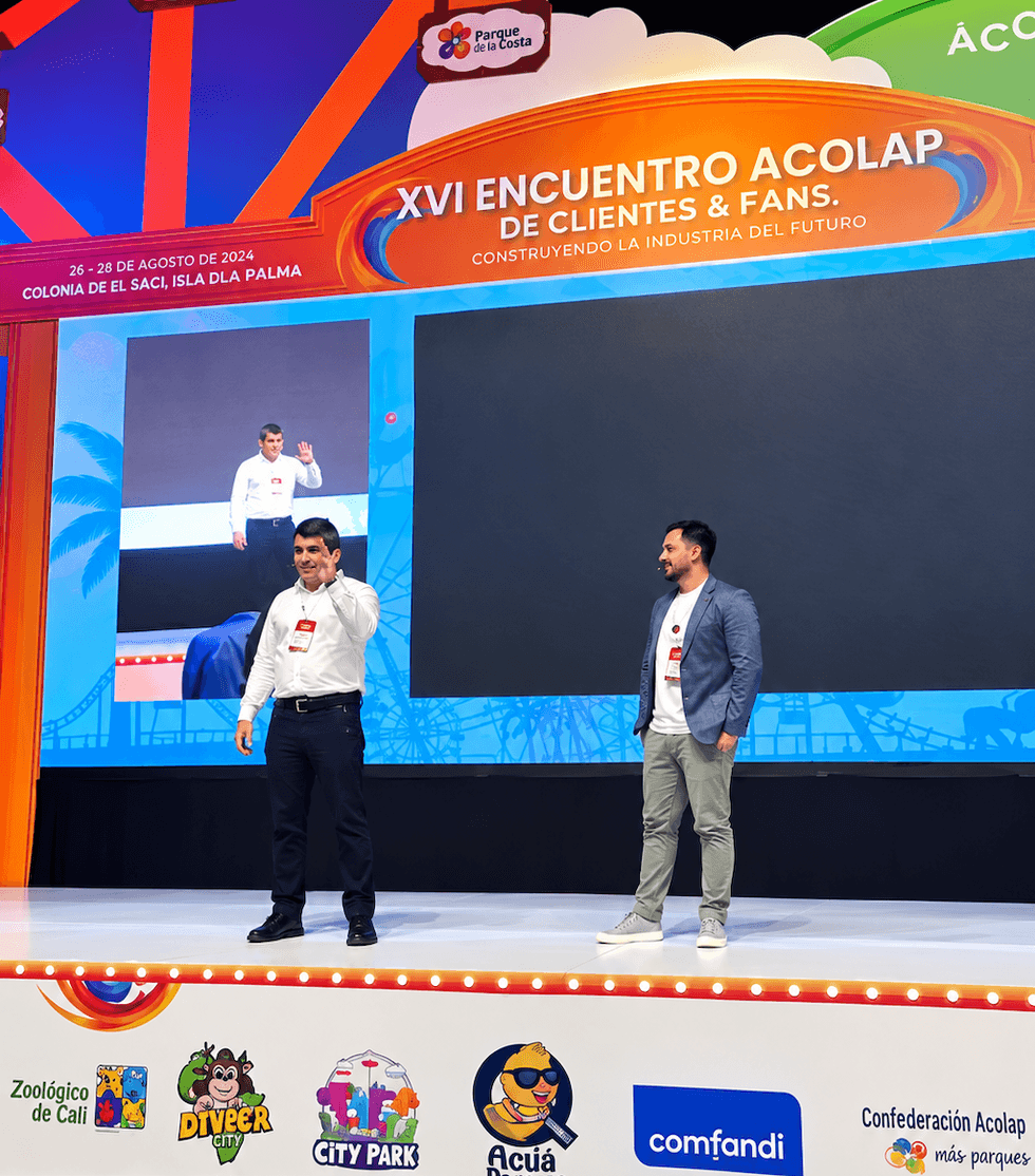 Two men on stage at Acolap event with colorful backdrop, logo, and screen.