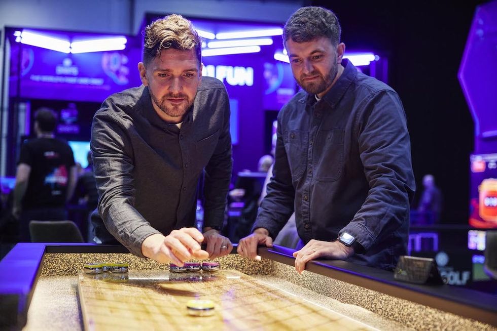 Two men playing a tabletop game from 501 Fun in a brightly lit arcade setting.