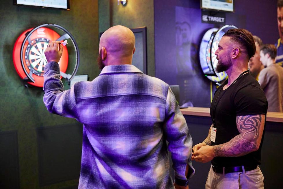 Two men playing darts indoors; one prepares to throw.