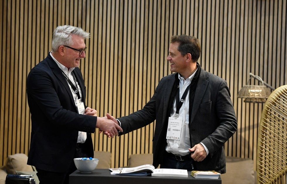 Two men shaking hands and smiling in a professional setting.