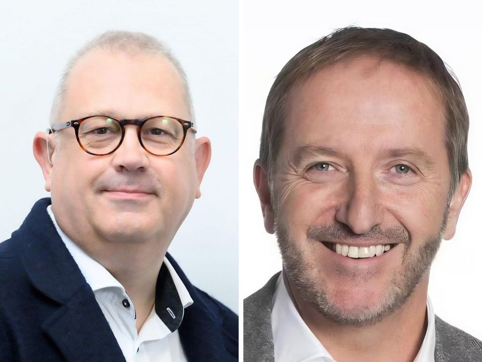 Two men side by side; one with glasses, the other with a beard, both smiling lightly.