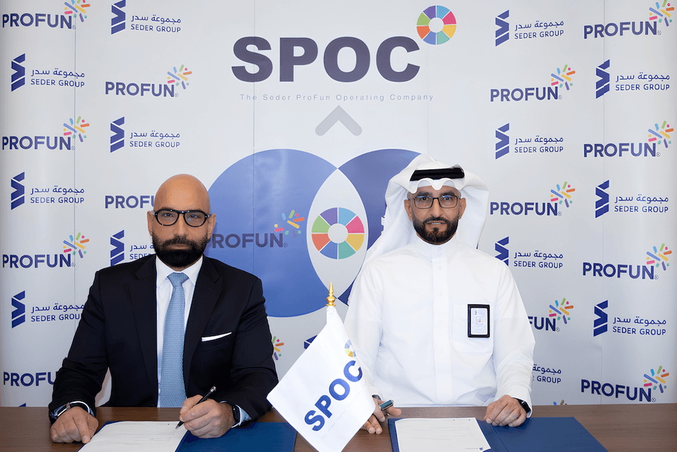 Two men sitting at a table with SPOC and PROFUN banners in the background.