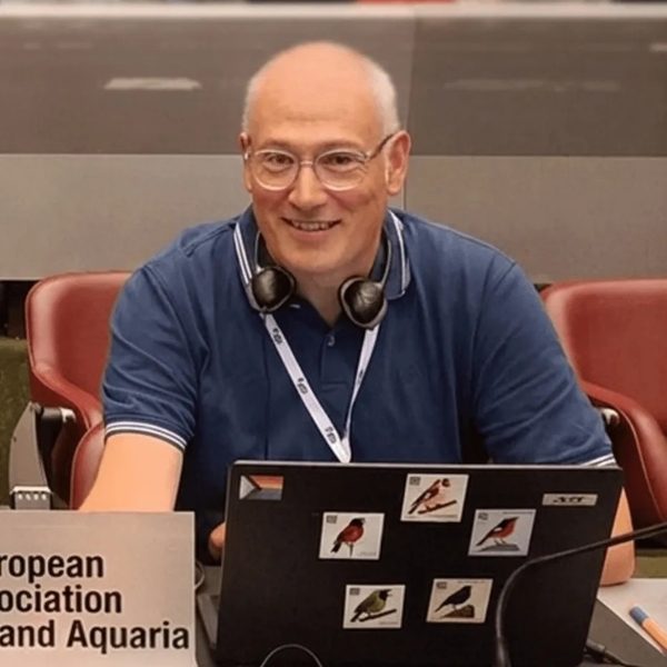 Two men smiling at a conference table with laptops and nameplate.