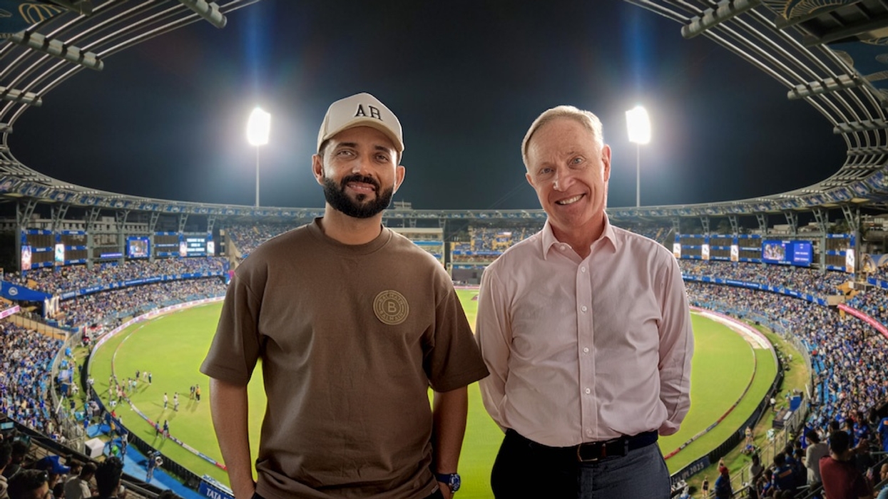 Two men smiling at a cricket stadium under bright lights.