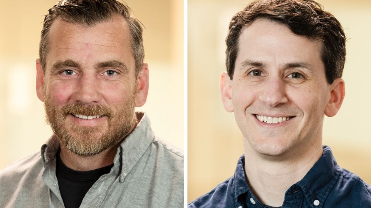 Two men smiling, one with a beard and gray shirt, the other clean-shaven in a navy shirt.