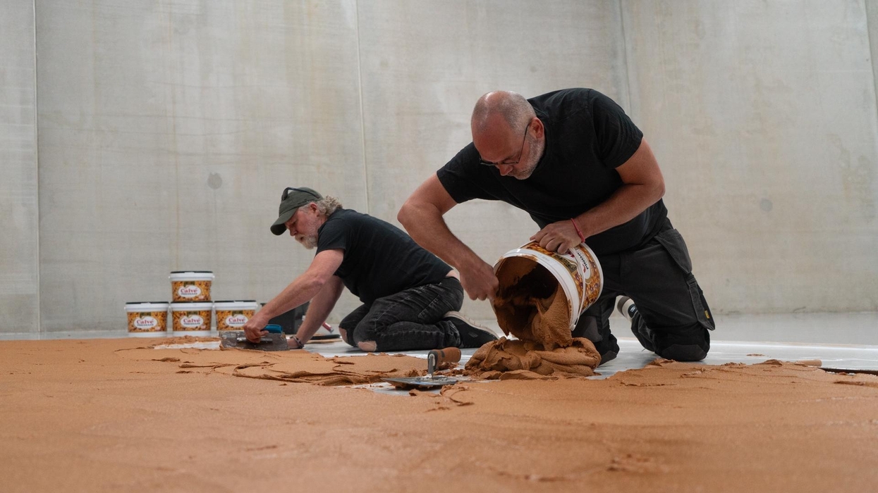 Two men spreading peanut butter on a concrete floor with buckets and tools at Museum Boijmans Van Beuningen