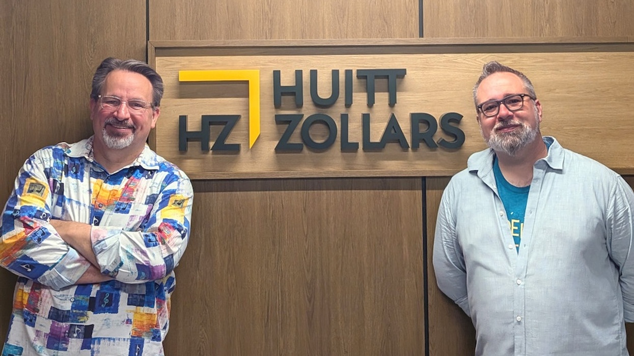 Two men stand smiling in front of the Huitt-Zollars office sign.