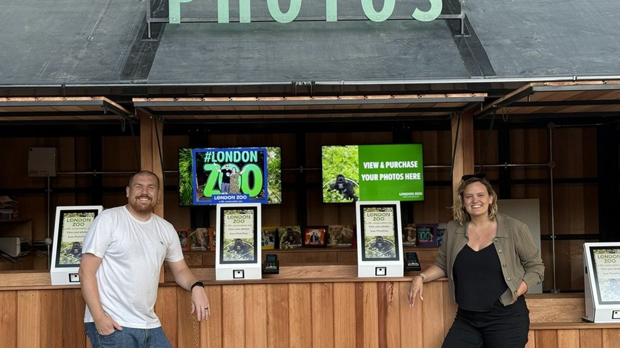 Two people at a London Zoo photo booth counter with signs promoting photo purchase.