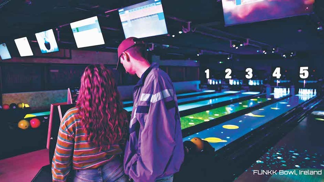 Two people at a vibrant bowling alley with glowing lanes and overhead screens.
