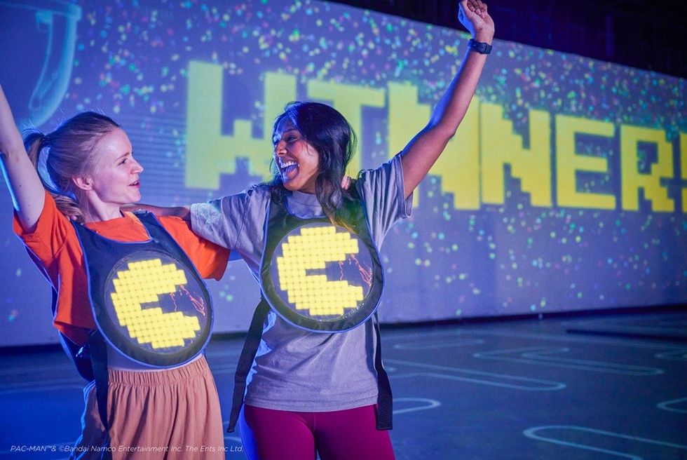 Two people celebrating in front of a large "WINNER!" sign, wearing Pac-Man outfits.