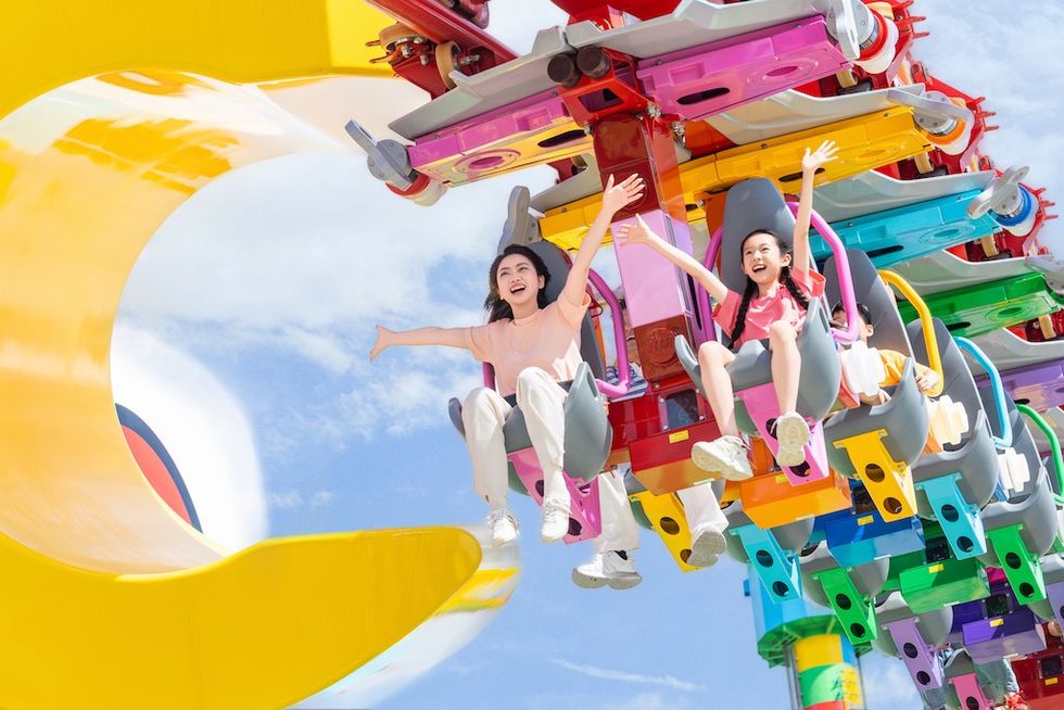 Two people enjoy a colorful roller coaster ride at Legoland Shanghai under a clear blue sky.