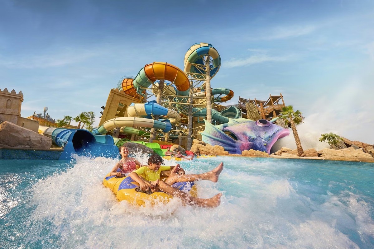 Two people enjoy a ride down a vibrant water slide at Yas Waterworld