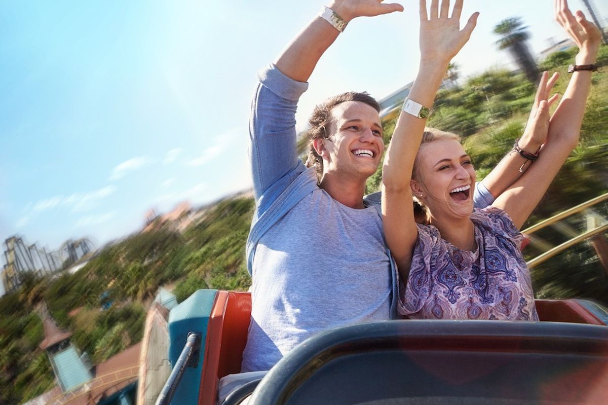 Two people enjoying a roller coaster ride with hands up.