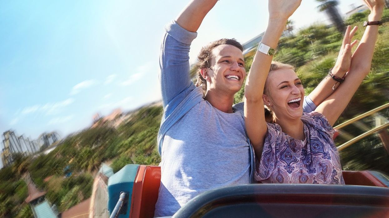 Two people enjoying a roller coaster ride with hands up.