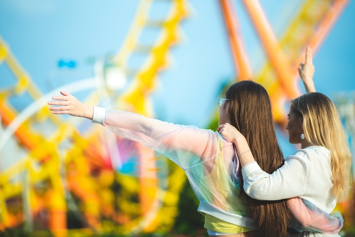 Two people enjoying a theme park, with roller coasters in the background.