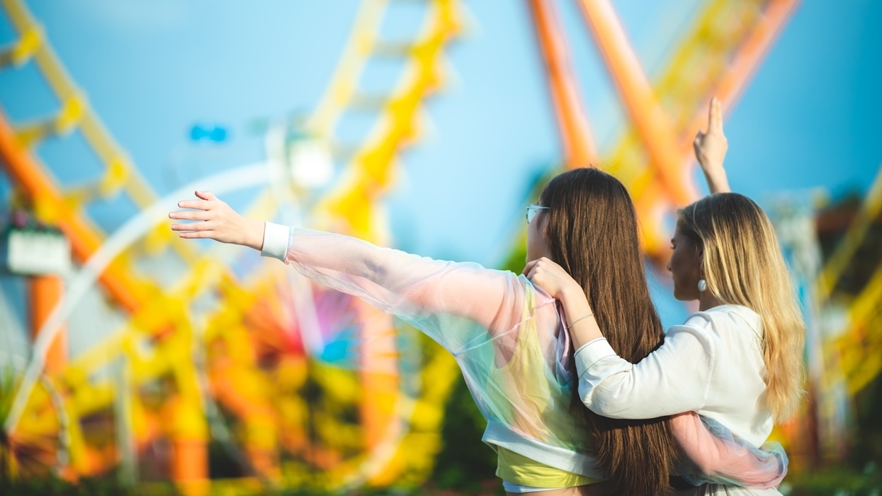 Two people enjoying a theme park, with roller coasters in the background.