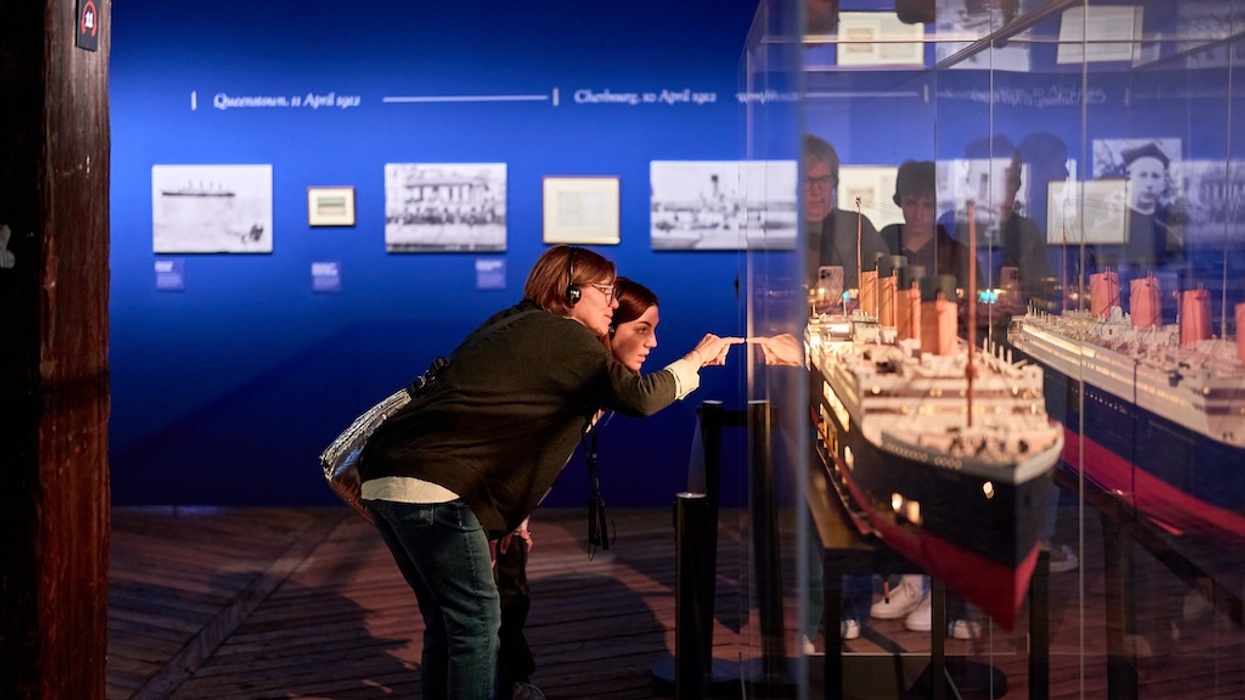 Two people examine a ship model in a museum exhibit with blue walls.