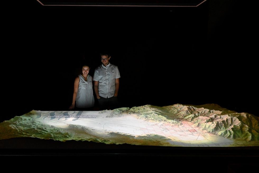 Two people examine an illuminated topographic model in a dark room Agua Caliente Cultural Museum RLMG