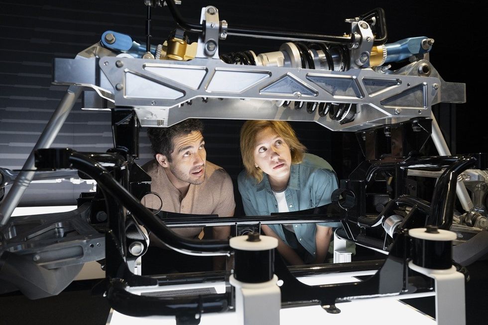 Two people examine the inner mechanics of a vehicle chassis.