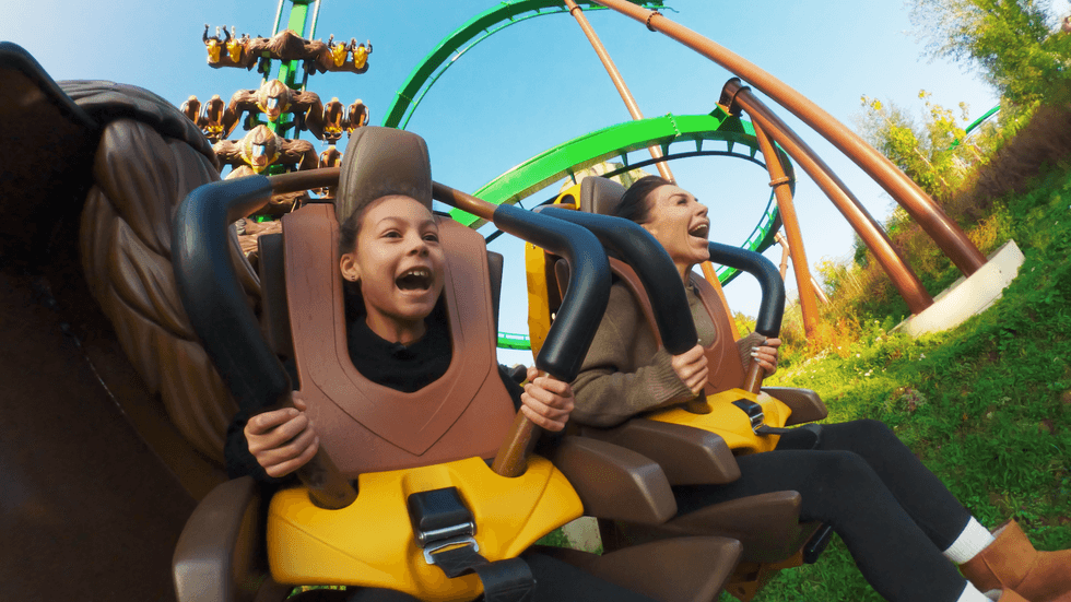Two people excitedly riding a roller coaster with green tracks in the background.