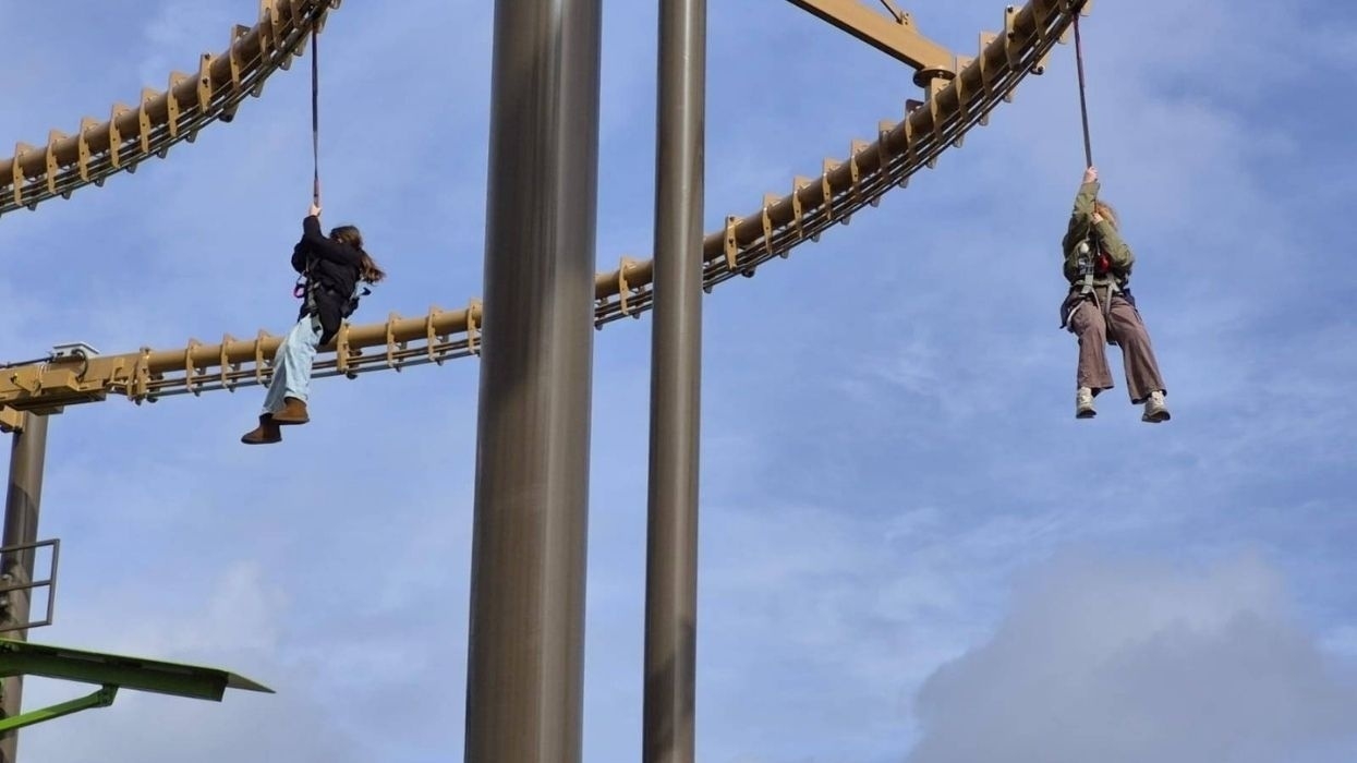 Two people hanging from a zipline ride under a blue sky at Universe Science Park in Denmark.