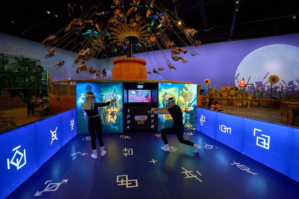 Two people in a VR arcade with vibrant decorations and a swing ride above.
