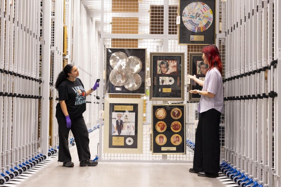 Two people in gloves examine framed music awards in a storage facility at the David Bowie Centre