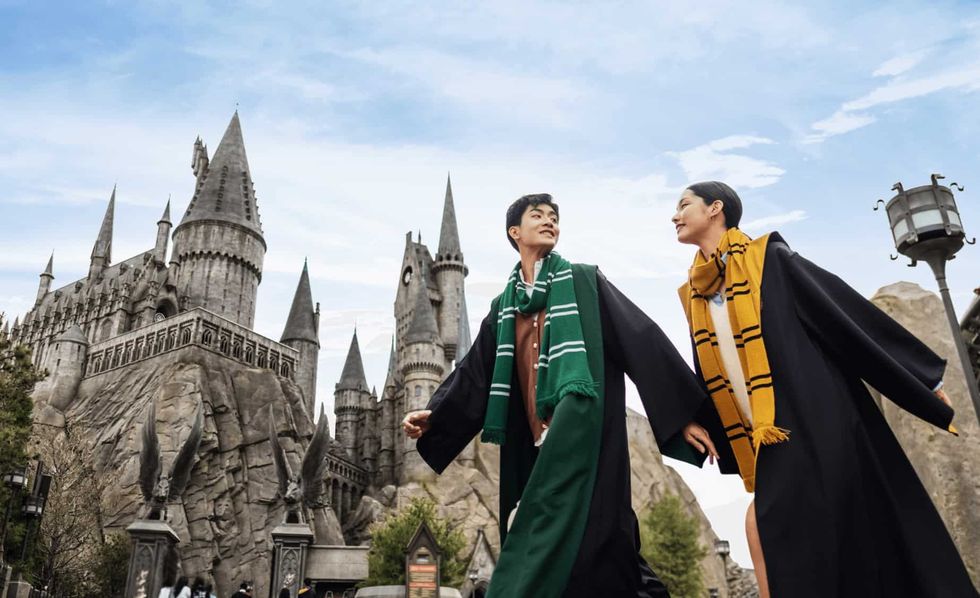 Two people in robes and scarves walking by a castle with spires at Universal Beijing