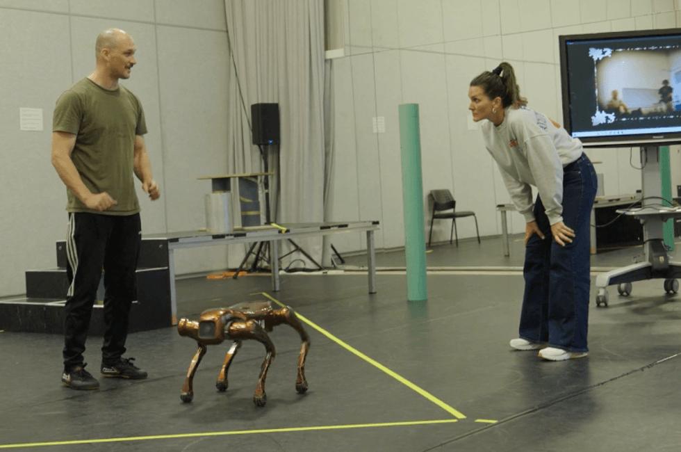Two people interact with a robotic dog in a rehearsal space.