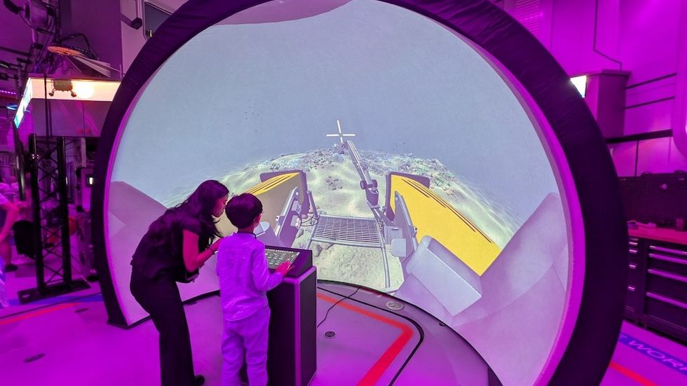 Two people interact with a virtual landscape on a large curved screen.