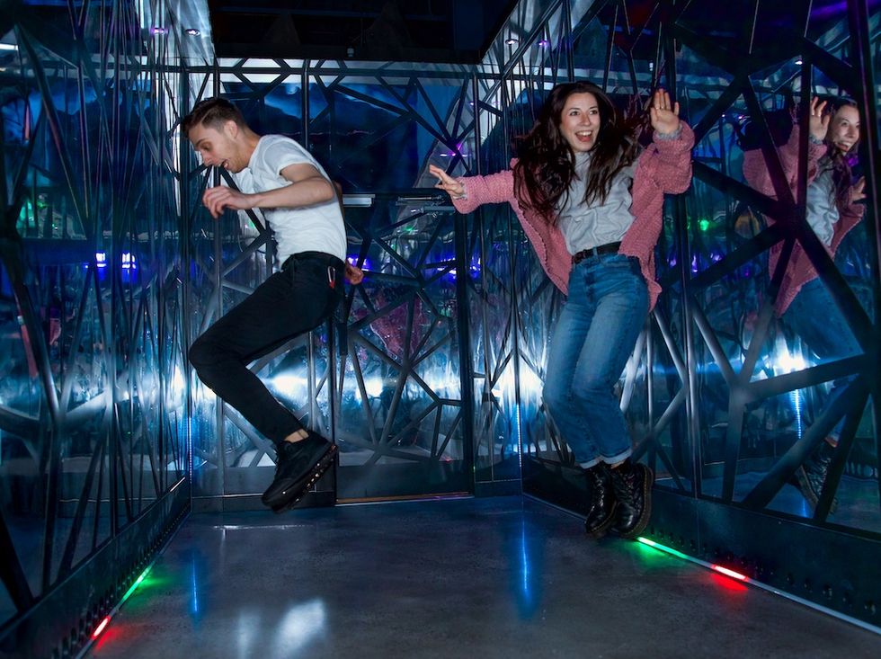 Two people joyfully jump in a mirrored room with colorful lights at Level99