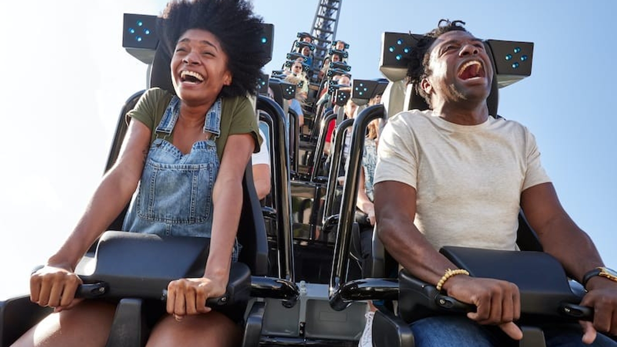 Two people joyfully riding a roller coaster, Velocicoaster, under a clear blue sky.