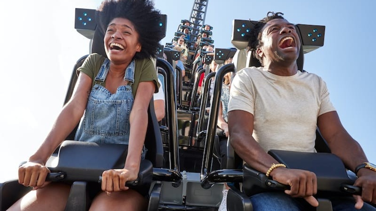 Two people joyfully riding a roller coaster, Velocicoaster, under a clear blue sky.