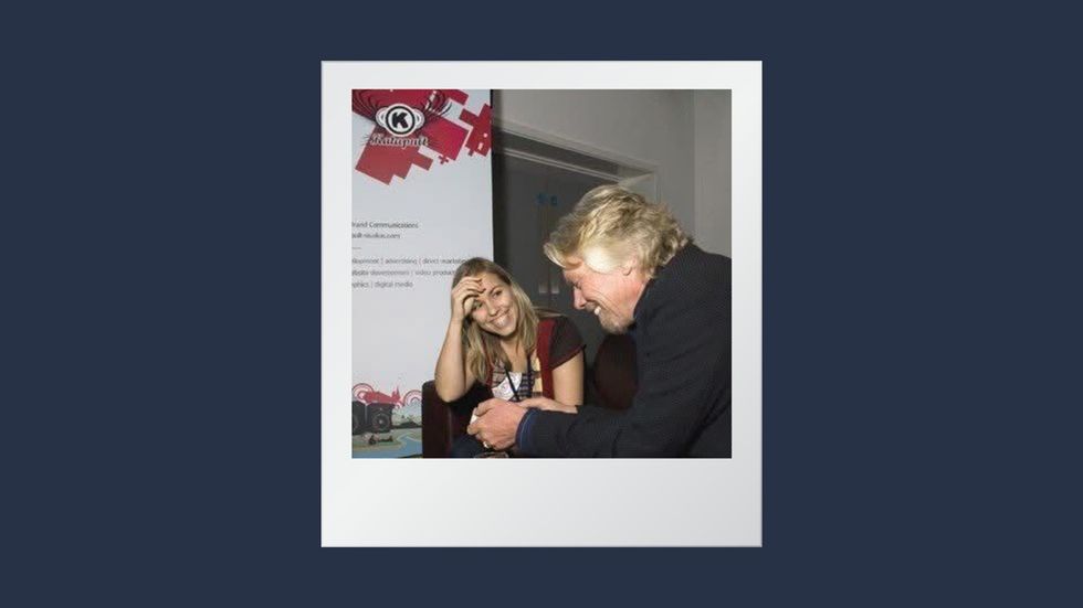 Two people laughing and talking near a promotional backdrop.