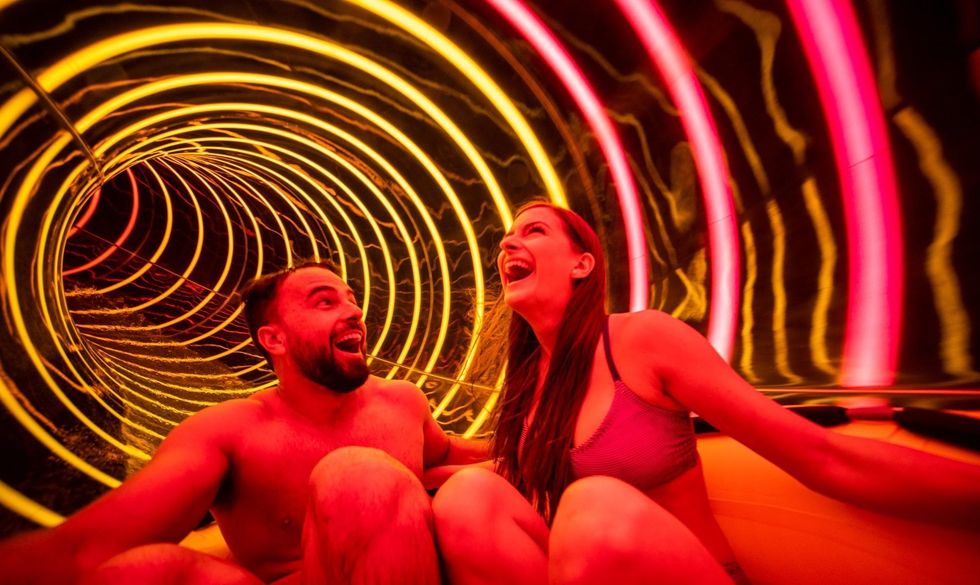 Two people laughing, sliding in a brightly lit tube water slide at Water Country USA